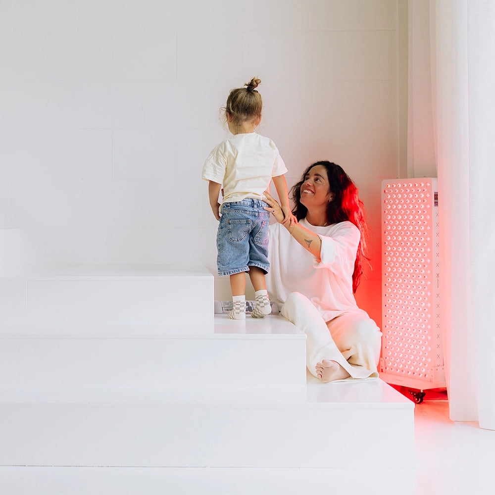 Vrouw met kind naast de Liroma Elite rood licht therapie lamp in de woonkamer